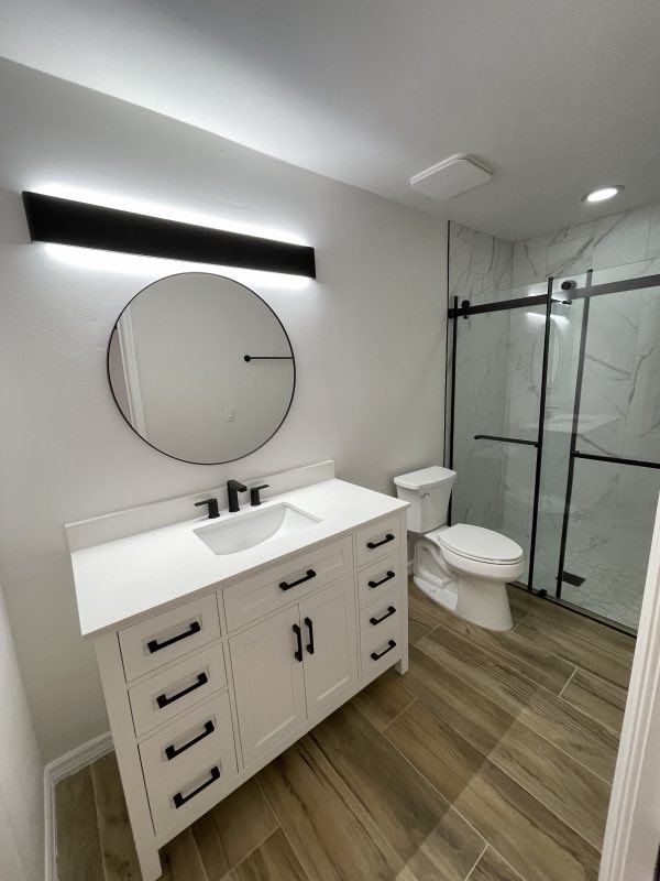 Modern bathroom with white vanity, round mirror and glass shower