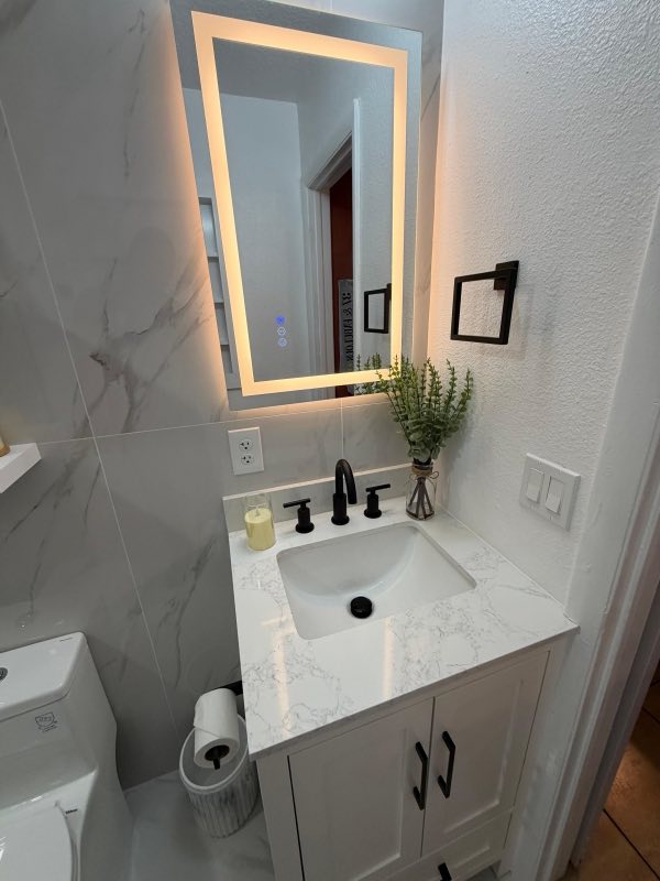 Marble powder room with backlit LED mirror and black fixtures